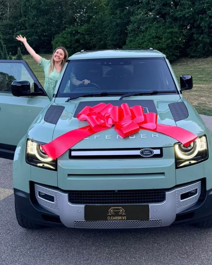 A customer waving from her new Land Rover Defender, finished with a red bow