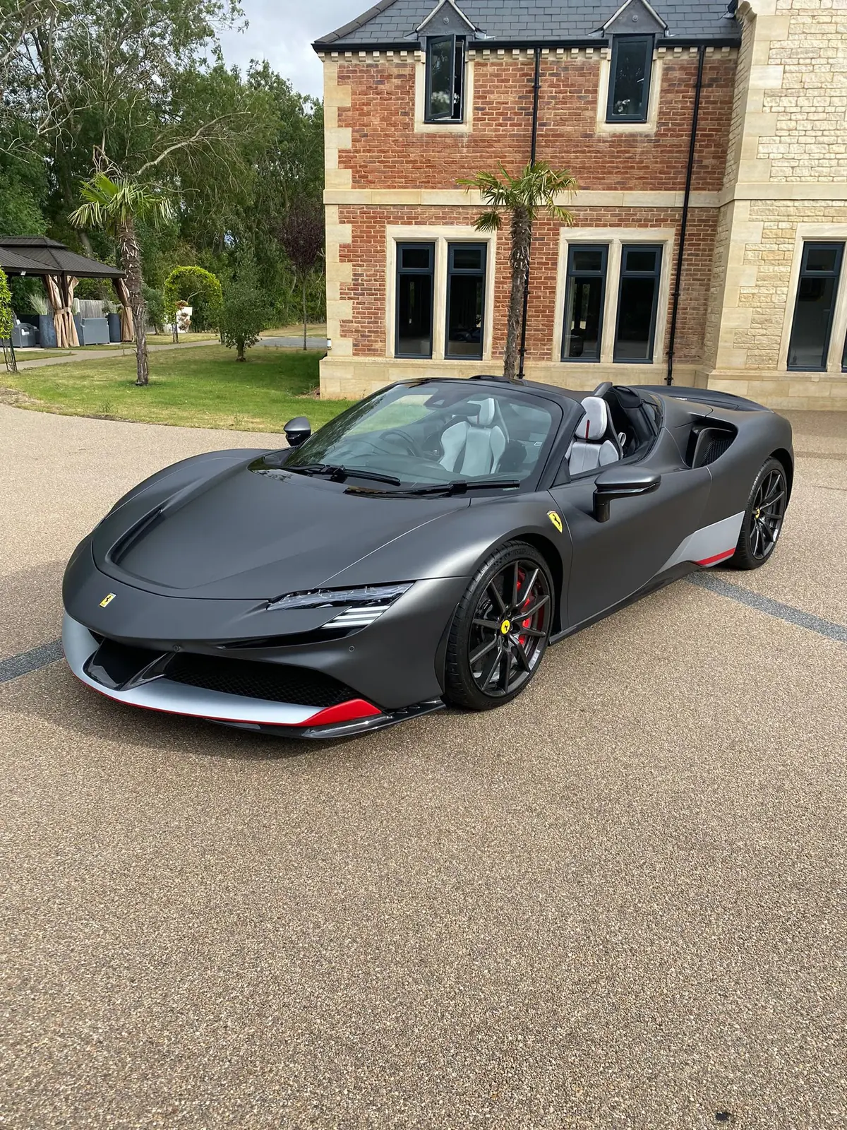 Matte grey Ferrari SF90 Spider parked on a gravel drive